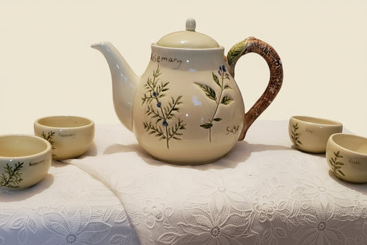Ceramic teapot and cups with floral design on a tablecloth.
